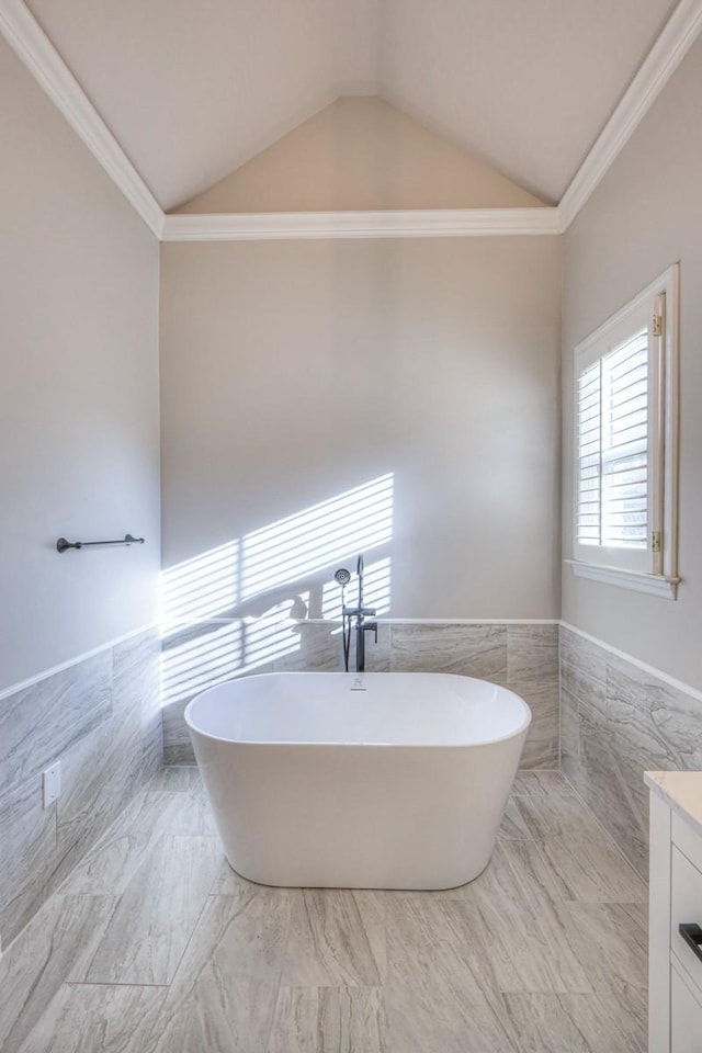 bathroom featuring a washtub, vanity, vaulted ceiling, crown molding, and tile walls