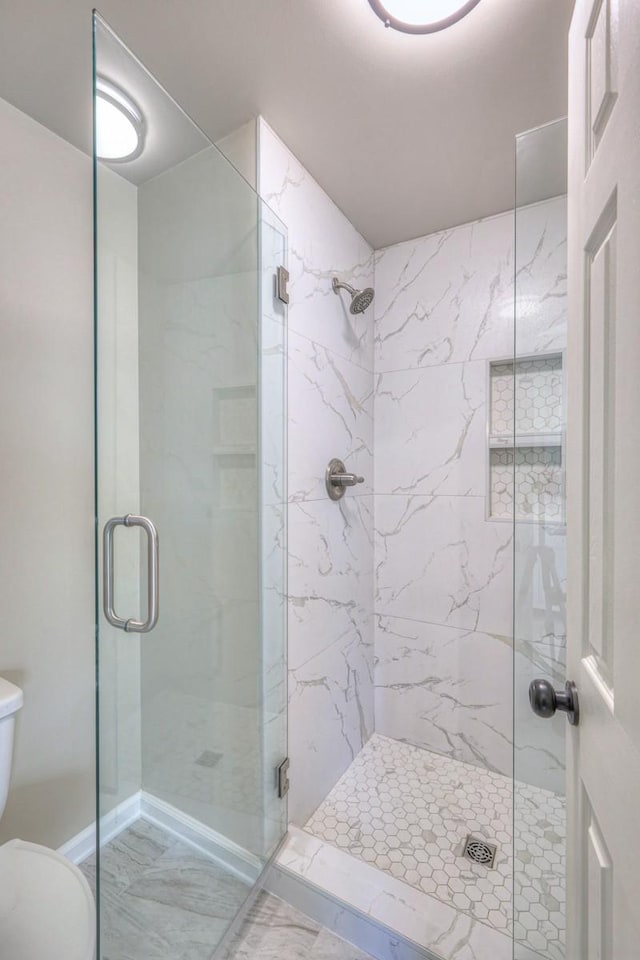 bathroom featuring a shower with shower door and toilet