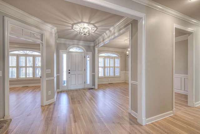 foyer entrance with plenty of natural light, light hardwood / wood-style flooring, a notable chandelier, and ornamental molding