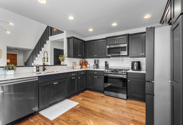 kitchen featuring light stone countertops, appliances with stainless steel finishes, backsplash, sink, and light hardwood / wood-style floors