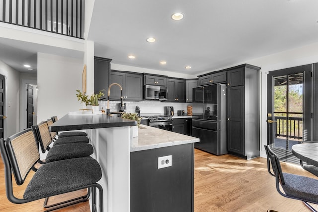 kitchen featuring a breakfast bar area, decorative backsplash, light stone countertops, light wood-type flooring, and stainless steel appliances