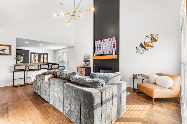 living room with a fireplace, a towering ceiling, wood-type flooring, and an inviting chandelier