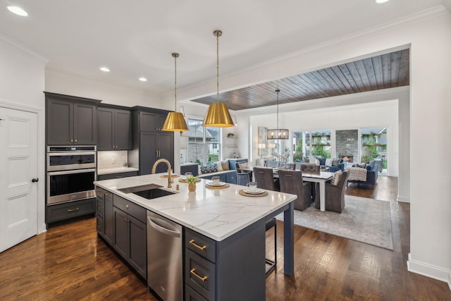 kitchen featuring dark wood-type flooring, sink, hanging light fixtures, an island with sink, and appliances with stainless steel finishes