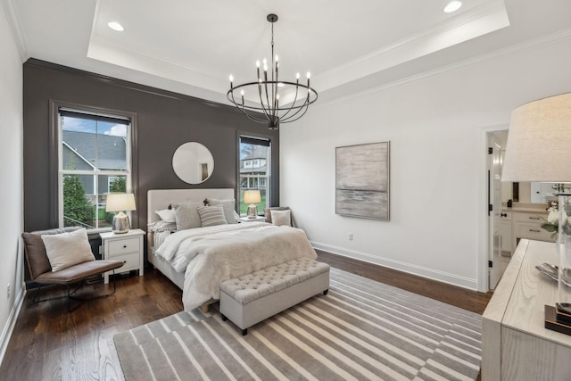 bedroom featuring ensuite bath, a tray ceiling, crown molding, dark wood-type flooring, and an inviting chandelier