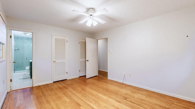 unfurnished bedroom featuring ensuite bathroom, light hardwood / wood-style flooring, ceiling fan, and two closets