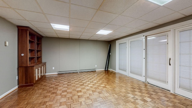 basement with a paneled ceiling, a baseboard heating unit, and light parquet flooring