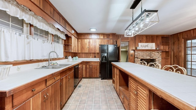 kitchen featuring black appliances, sink, wooden walls, a brick fireplace, and decorative light fixtures