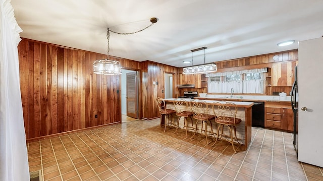 kitchen featuring sink, wooden walls, black dishwasher, a kitchen island, and a breakfast bar area