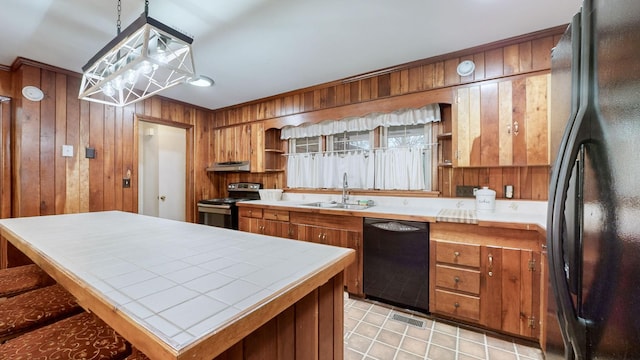 kitchen with extractor fan, wooden walls, sink, black appliances, and hanging light fixtures