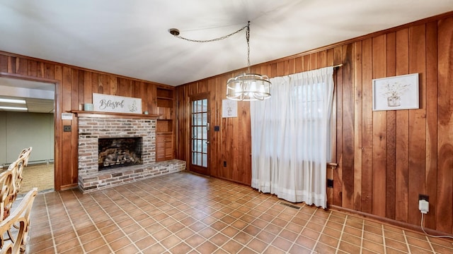 unfurnished living room with a baseboard heating unit, a brick fireplace, a notable chandelier, and wood walls