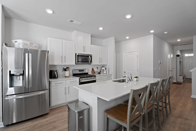 kitchen with a center island with sink, white cabinetry, hardwood / wood-style floors, and appliances with stainless steel finishes