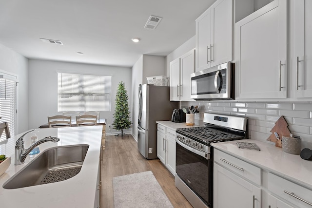 kitchen featuring white cabinetry, sink, backsplash, light hardwood / wood-style floors, and appliances with stainless steel finishes