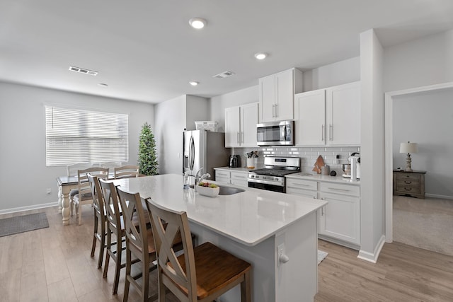 kitchen with white cabinets, a center island with sink, a breakfast bar area, and appliances with stainless steel finishes