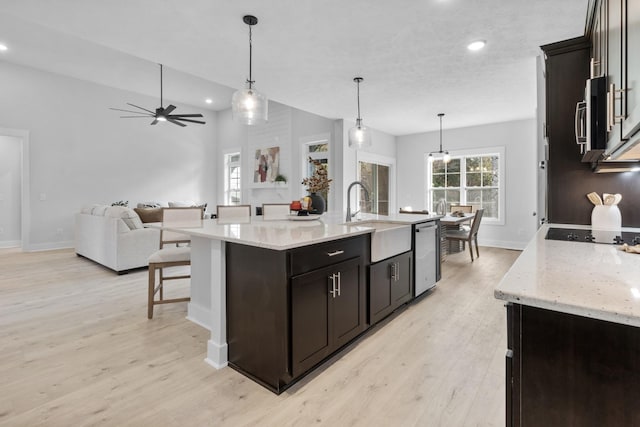 kitchen with decorative light fixtures, a center island with sink, stainless steel dishwasher, and sink