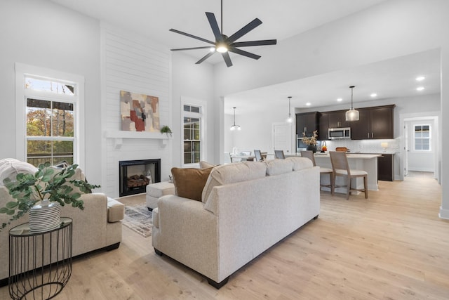 living room with a fireplace, a towering ceiling, light hardwood / wood-style flooring, and ceiling fan