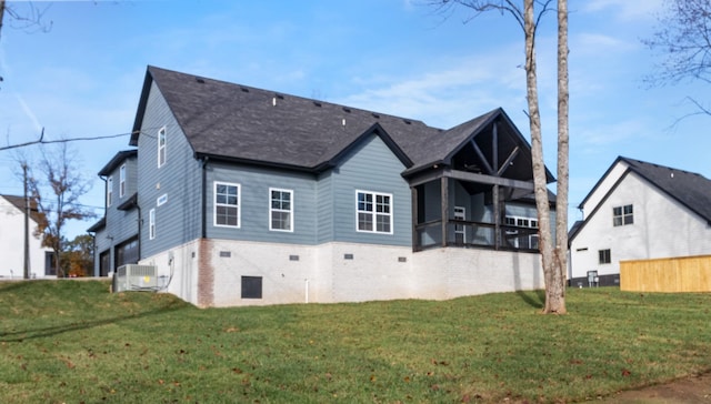 rear view of house featuring a sunroom, a garage, a lawn, and central AC