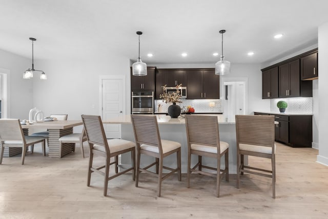 kitchen featuring appliances with stainless steel finishes, dark brown cabinetry, decorative light fixtures, and light hardwood / wood-style flooring