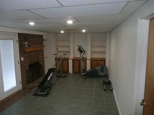 exercise room featuring tile patterned floors, a brick fireplace, and a drop ceiling