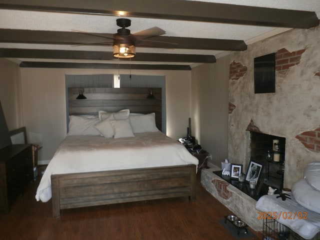 bedroom featuring dark hardwood / wood-style flooring, ceiling fan, beam ceiling, and a fireplace