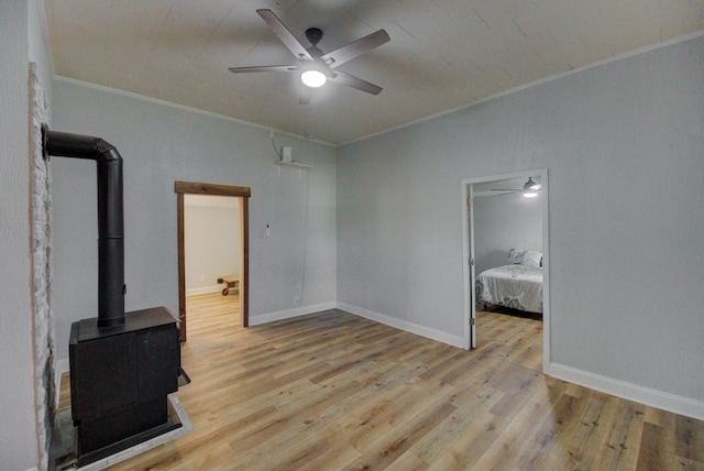 unfurnished living room featuring ceiling fan, light wood-type flooring, a wood stove, and crown molding