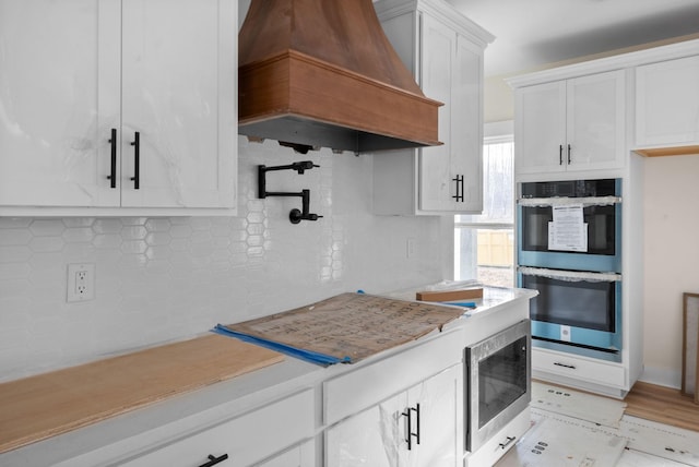 kitchen with appliances with stainless steel finishes, backsplash, premium range hood, and white cabinetry