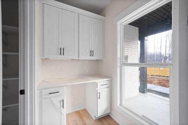 interior space featuring built in desk, light hardwood / wood-style flooring, white cabinetry, and a wealth of natural light