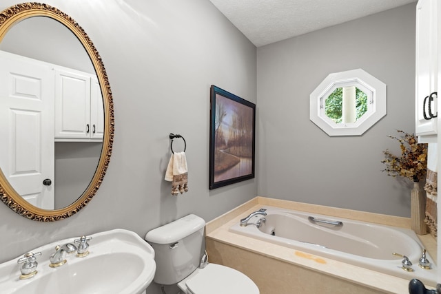 bathroom featuring a washtub, a textured ceiling, toilet, and sink