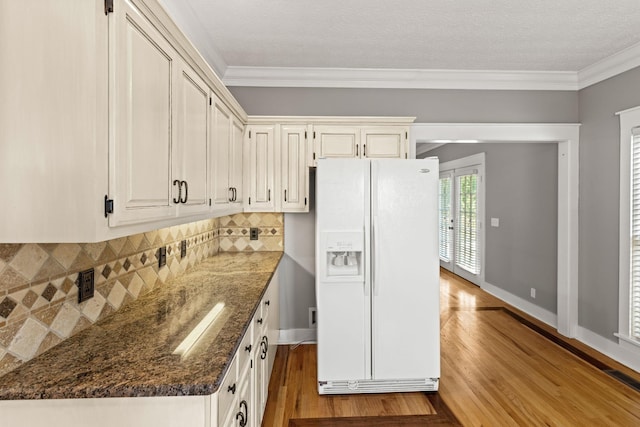 kitchen with white refrigerator with ice dispenser, ornamental molding, light hardwood / wood-style flooring, and dark stone counters