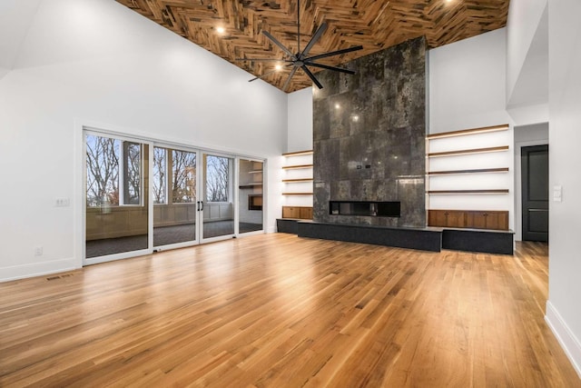 unfurnished living room featuring a towering ceiling, ceiling fan, wood-type flooring, wooden ceiling, and a premium fireplace