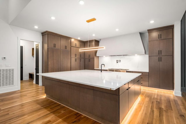 kitchen featuring a large island with sink, light hardwood / wood-style flooring, custom exhaust hood, and sink