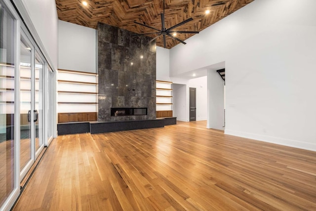 unfurnished living room featuring wooden ceiling, ceiling fan, a towering ceiling, a premium fireplace, and wood-type flooring