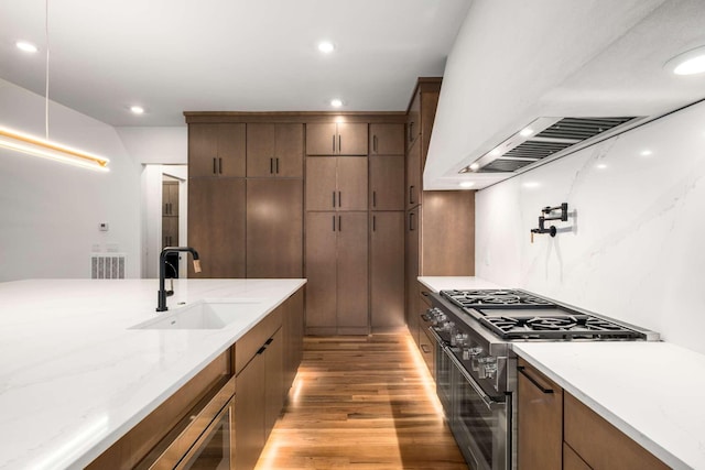 kitchen with light stone countertops, light wood-type flooring, high end black range, sink, and range hood