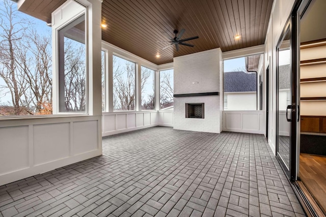 unfurnished sunroom featuring a brick fireplace, ceiling fan, and wooden ceiling