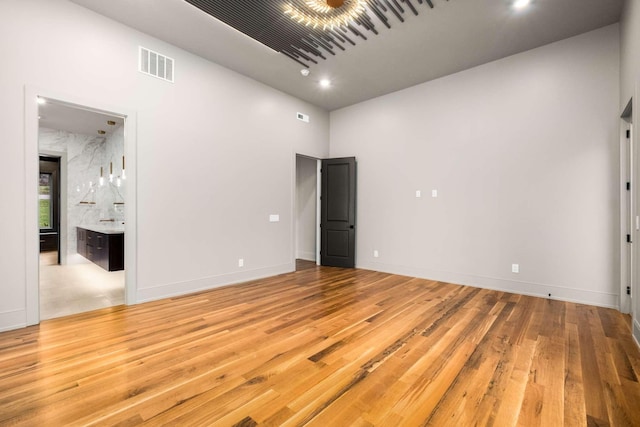 unfurnished bedroom with connected bathroom, light hardwood / wood-style flooring, and a towering ceiling