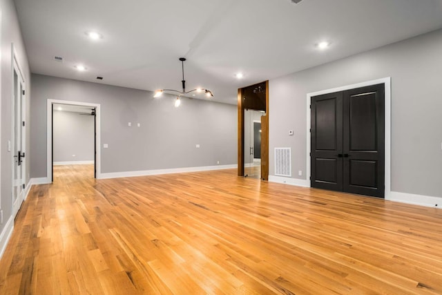 empty room with light wood-type flooring and a notable chandelier