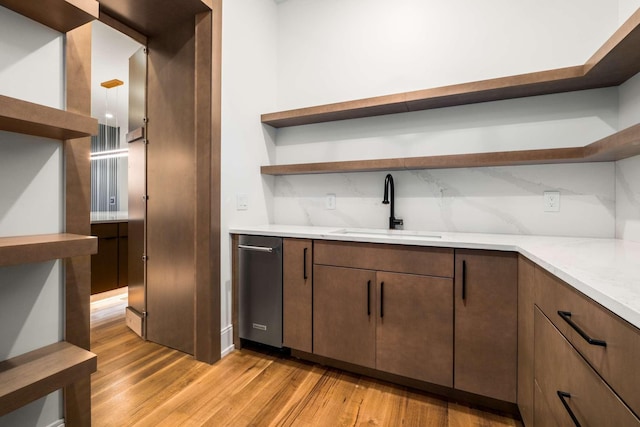 kitchen with dishwasher, light wood-type flooring, light stone countertops, and sink