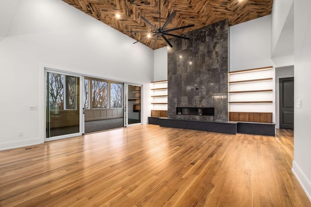 unfurnished living room with a towering ceiling, ceiling fan, hardwood / wood-style flooring, wooden ceiling, and a tiled fireplace