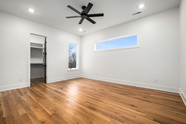 unfurnished bedroom featuring wood-type flooring, a walk in closet, a closet, and ceiling fan