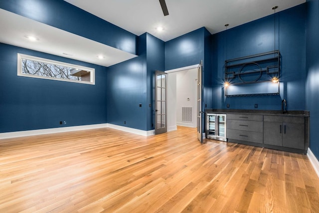 interior space featuring sink, ceiling fan, a towering ceiling, light hardwood / wood-style floors, and beverage cooler