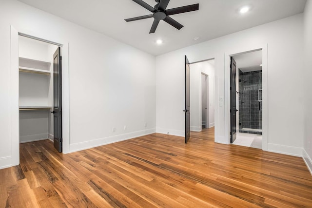 unfurnished bedroom featuring ensuite bathroom, ceiling fan, wood-type flooring, and a spacious closet