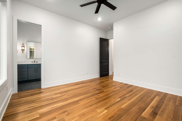 unfurnished bedroom featuring ceiling fan, sink, light wood-type flooring, and ensuite bathroom