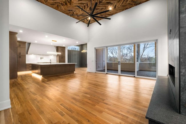 unfurnished living room featuring a towering ceiling, light hardwood / wood-style floors, ceiling fan, and wood ceiling