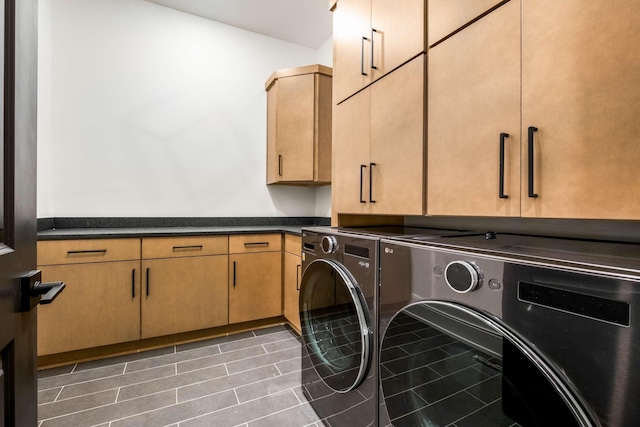 laundry room featuring washing machine and clothes dryer, dark tile patterned floors, and cabinets