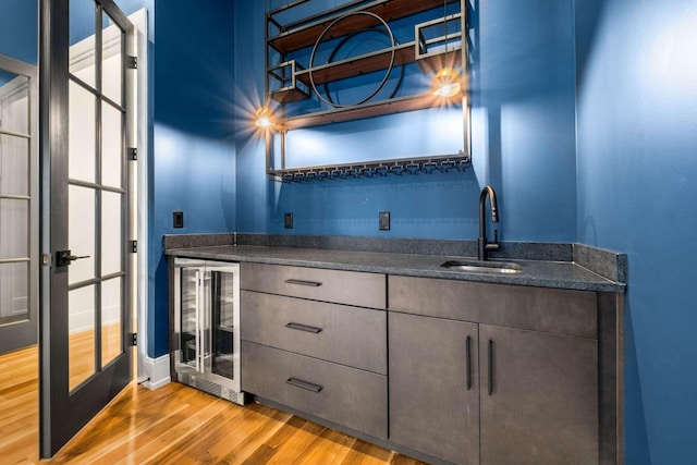 bar featuring light wood-type flooring, sink, and beverage cooler