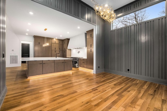 kitchen featuring premium range hood, a large island with sink, hanging light fixtures, light wood-type flooring, and high end stove