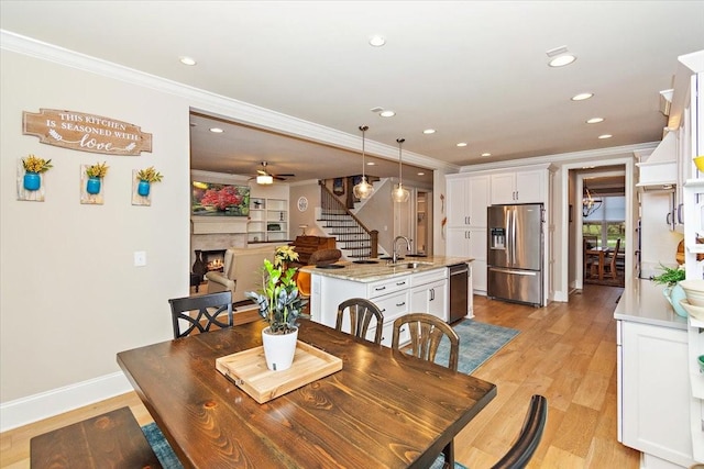 dining space with ceiling fan, sink, ornamental molding, and light wood-type flooring