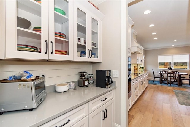 bar featuring cooktop, white cabinets, ornamental molding, and light wood-type flooring