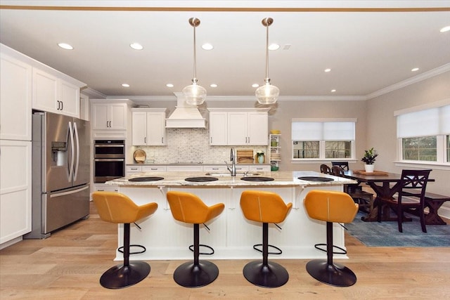 kitchen featuring white cabinets, hanging light fixtures, light wood-type flooring, an island with sink, and appliances with stainless steel finishes