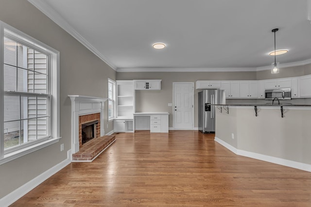 unfurnished living room featuring plenty of natural light, ornamental molding, and light hardwood / wood-style flooring