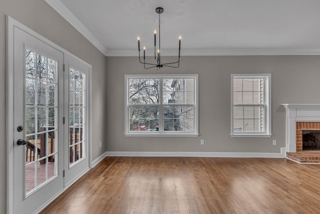 unfurnished dining area with hardwood / wood-style flooring, a brick fireplace, a notable chandelier, and crown molding